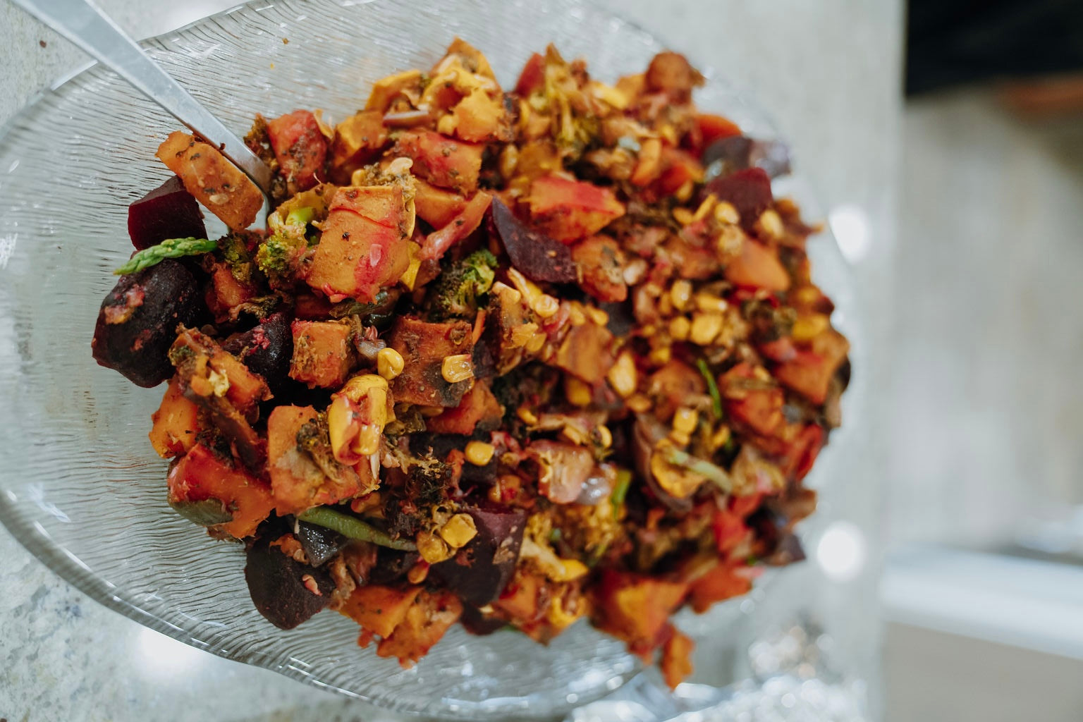 Glass bowl filled with a colorful mix of chopped vegetables and possibly meat on a light background.